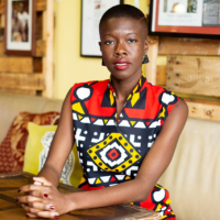 Nadege Green seated, wearing a bold graphic print of red, yellow, black, and white