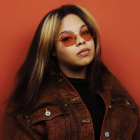 Paige Wood wearing red tinted glasses and a red jacket in front of a red background
